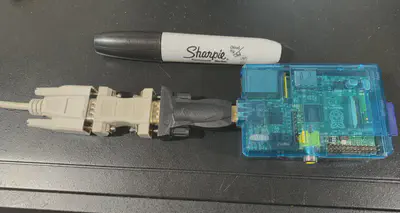 A serial cable plugged into a null modem adapter, which in turn is plugged into a USB to serial adapter, which in turn is plugged into a Raspberry Pi.